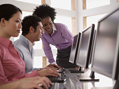 A woman leader helping her employees who are sitting at a computer.