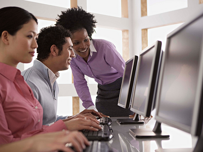 A woman leader helping her employees who are sitting at a computer. 