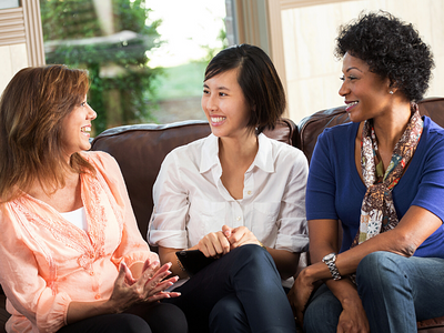 Three coworkers sitting together on a couch having a casual conversation with each other and smiling.