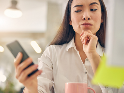 Woman holding her phone looking skeptically at it.